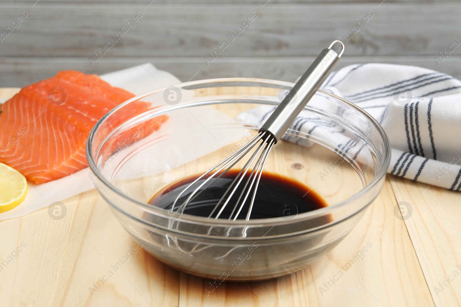 Photo of Soy sauce in bowl, whisk and salmon fillet on wooden table, closeup