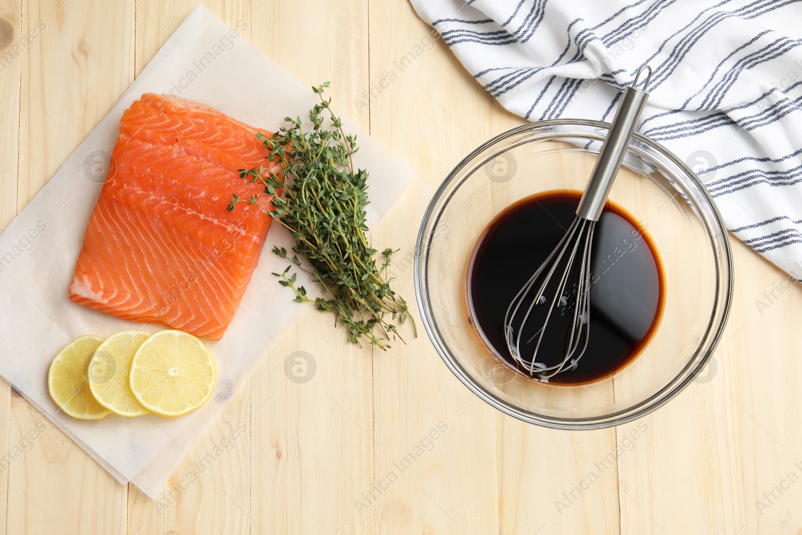 Photo of Soy sauce in bowl, whisk, salmon fillet, thyme and lemon slices on wooden table, flat lay