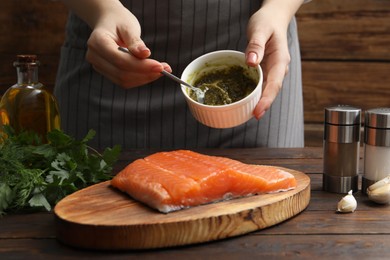 Photo of Woman marinating salmon fillet at wooden table, closeup