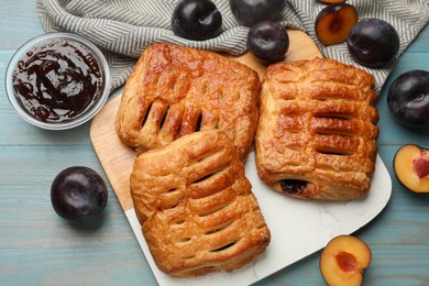 Photo of Delicious puff pastries, jam and plums on light blue wooden table, top view