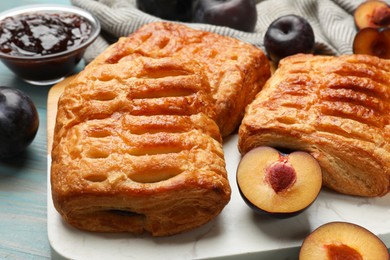 Delicious puff pastries and plums on light blue wooden table, closeup