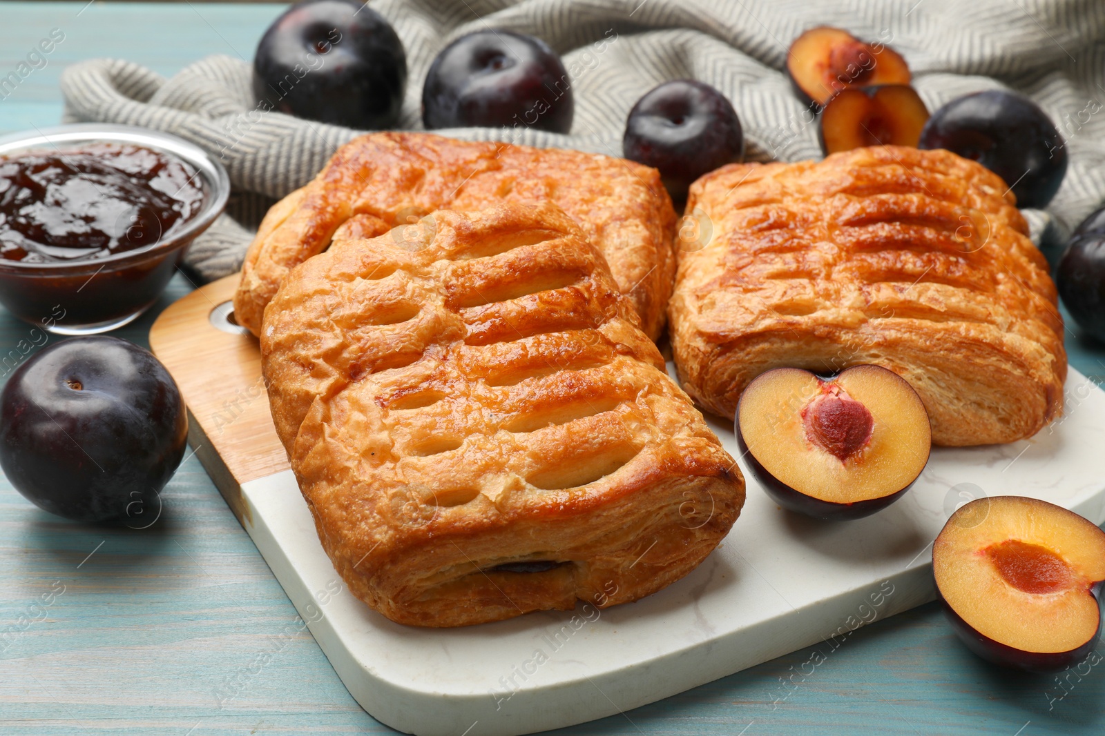 Photo of Delicious puff pastries and plums on light blue wooden table, closeup