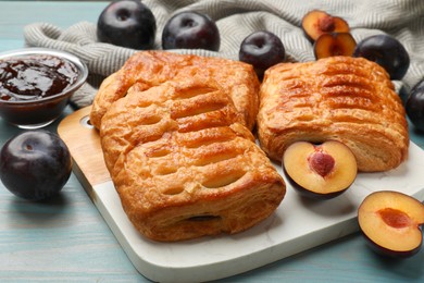 Photo of Delicious puff pastries and plums on light blue wooden table, closeup