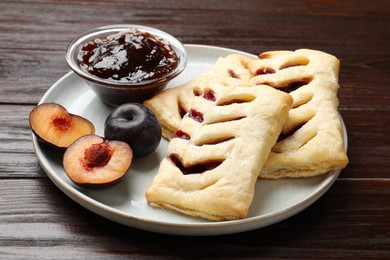 Photo of Delicious puff pastries, jam and plums on wooden table, closeup