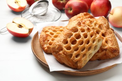 Photo of Delicious puff pastries, apples and powdered sugar on white table, closeup