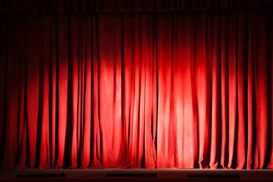 Photo of Elegant closed red curtains illuminated by spotlight in theatre