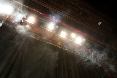 Photo of Professional spotlights and smoke on stage in theatre, low angle view