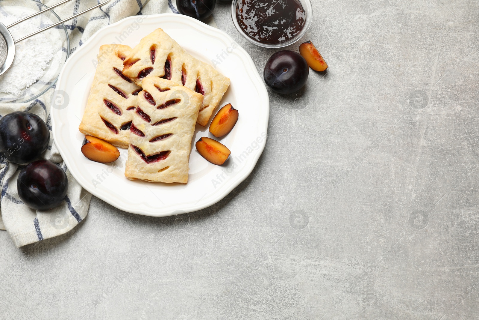 Photo of Delicious puff pastries, plums and jam on grey table, top view. Space for text