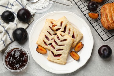 Photo of Delicious puff pastries, plums and jam on grey table, top view