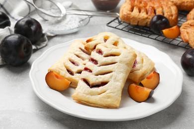 Photo of Delicious puff pastries and plums on grey table, closeup