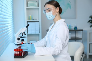 Photo of Laboratory testing. Doctor taking test tube with blood sample from rack at table indoors