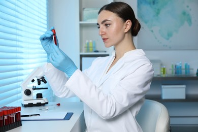 Photo of Laboratory testing. Doctor holding test tube with blood sample at table indoors