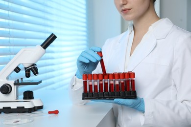 Photo of Laboratory testing. Doctor taking test tube with blood sample from rack indoors, closeup