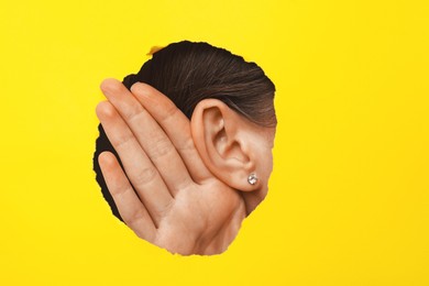 Woman showing hand to ear gesture through hole in yellow paper, closeup