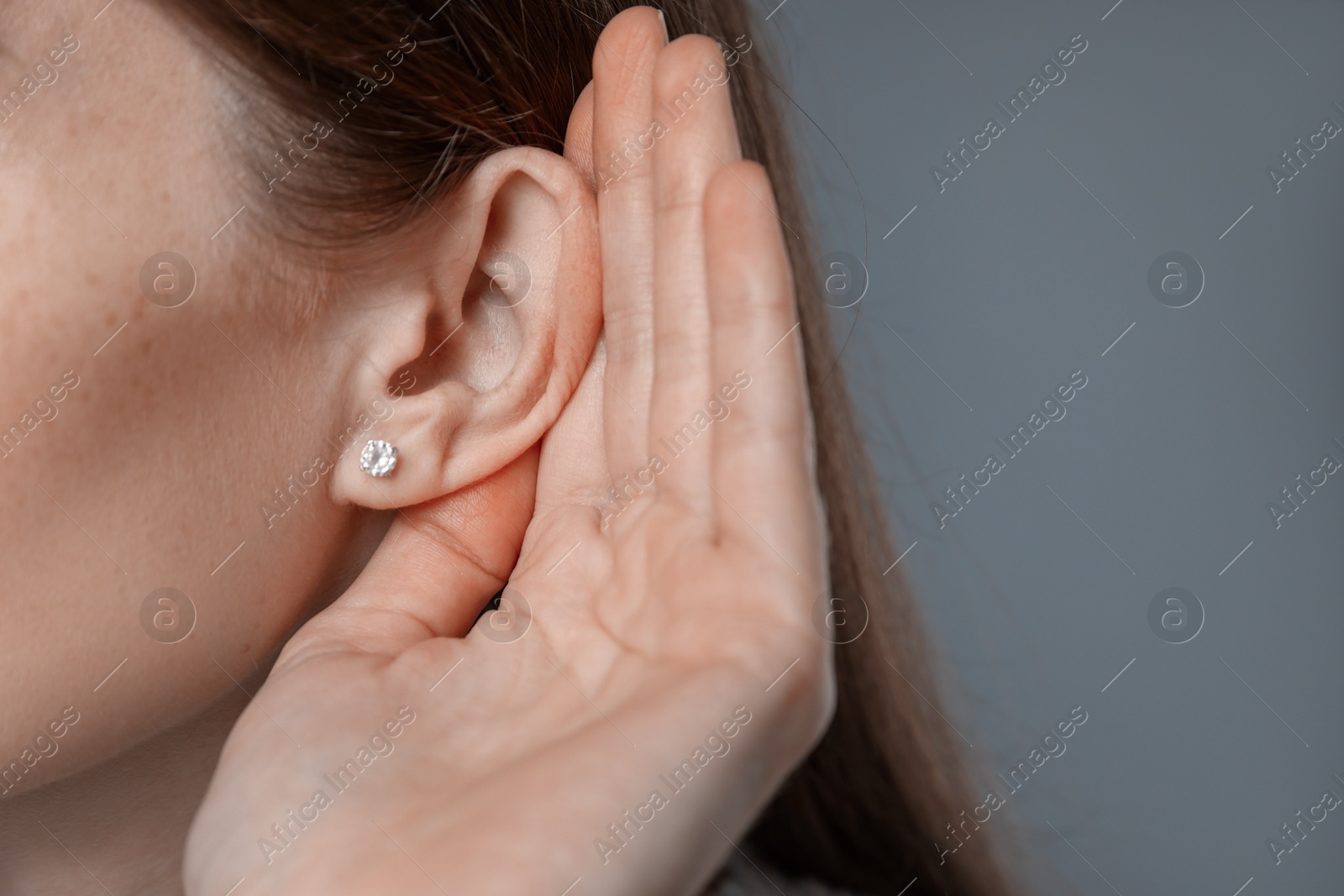 Photo of Woman showing hand to ear gesture on grey background, closeup. Space for text