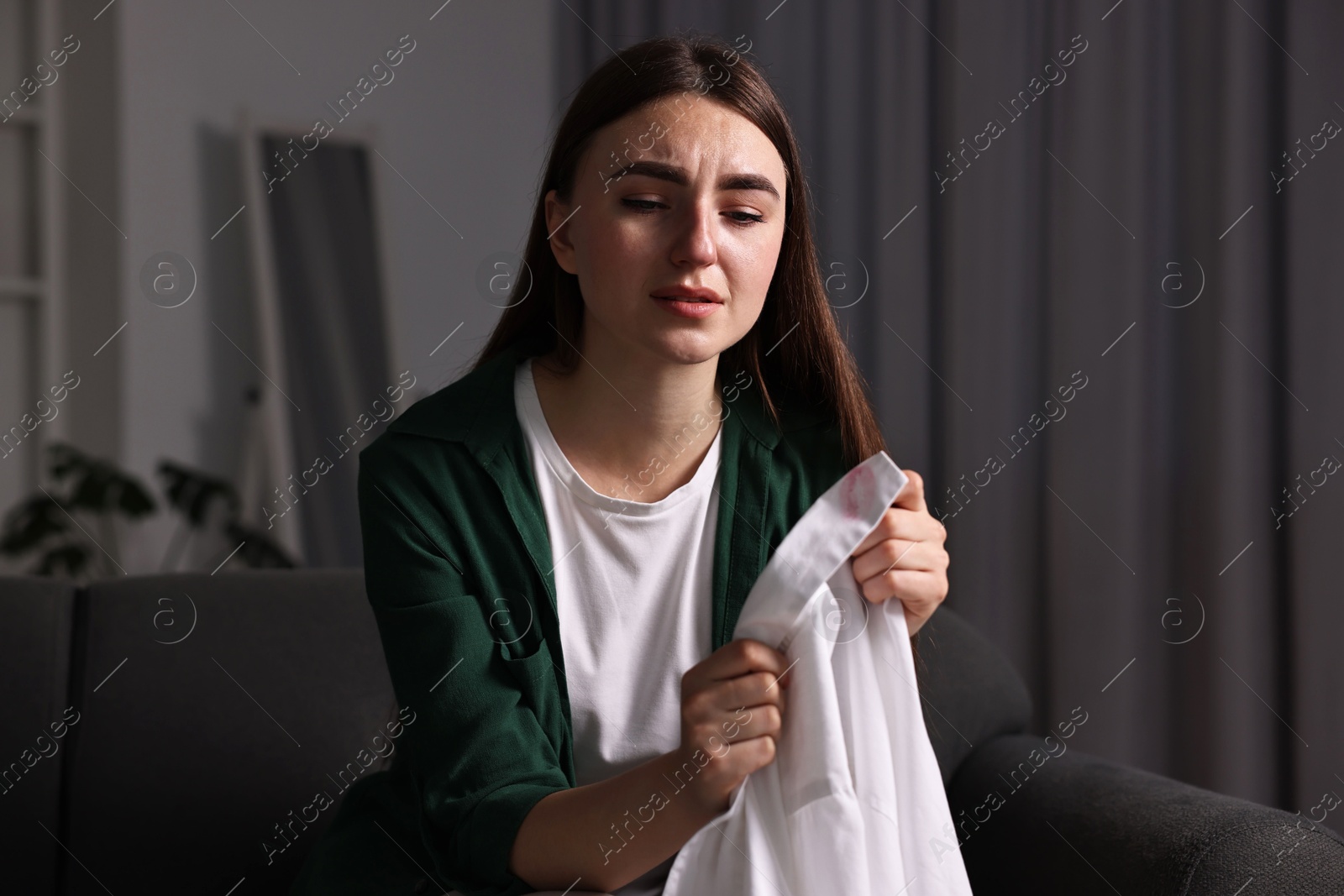 Photo of Frustrated wife holding shirt with lipstick marks as proof of her unfaithful husband at home