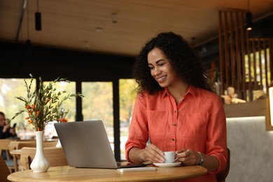 Photo of Woman with cup of coffee working on laptop in cafe