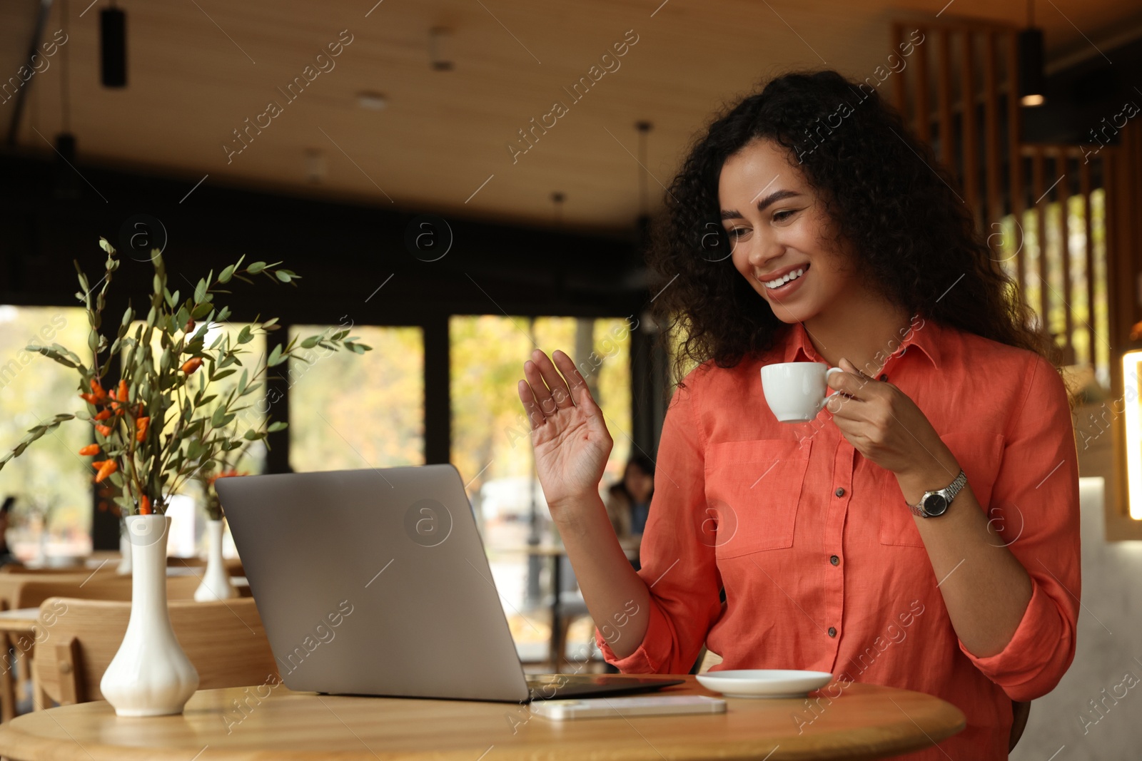 Photo of Woman with cup of coffee having video call in cafe