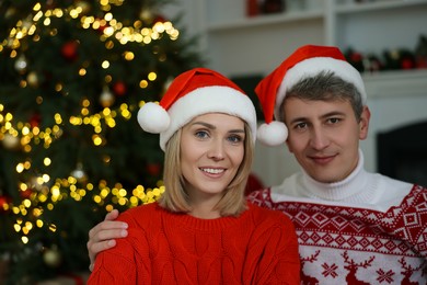 Photo of Lovely couple in Santa hats and Christmas sweaters at home