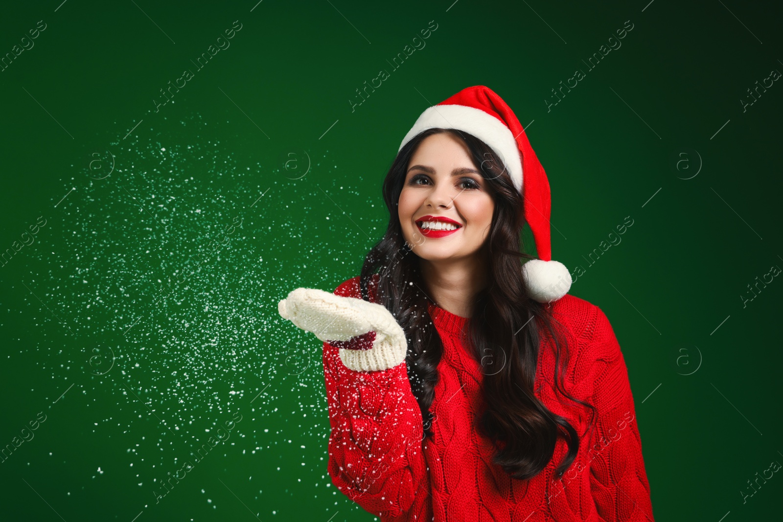 Photo of Attractive woman in Santa hat blowing snow off hands on green background. Christmas celebration