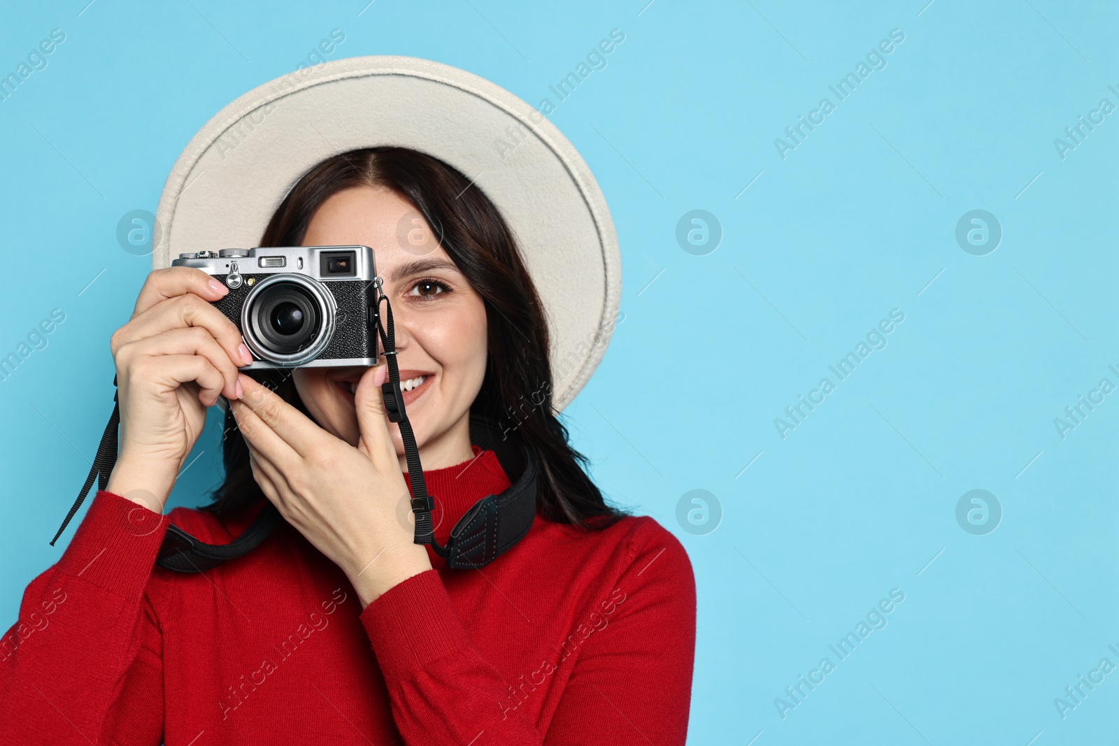 Photo of Young tourist in hat with camera on light blue background, space for text