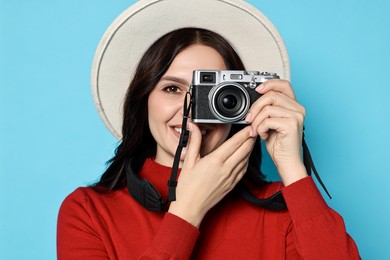 Young tourist in hat with camera on light blue background