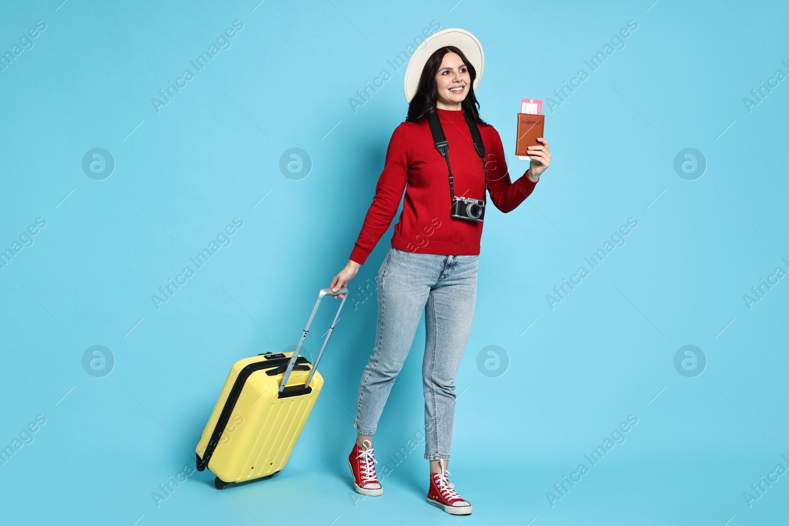 Photo of Young tourist in hat with camera, passport, tickets and suitcase on light blue background