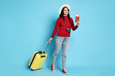 Photo of Young tourist in hat with camera, passport, tickets and suitcase on light blue background