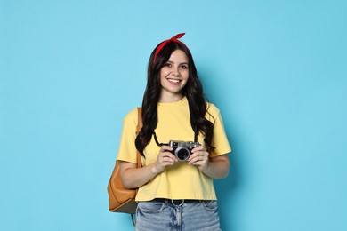 Photo of Young tourist with camera and backpack on light blue background