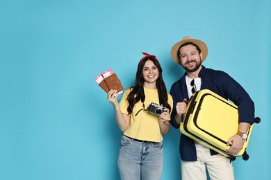 Photo of Tourism. Happy couple with passports, tickets and suitcase on light blue background, space for text