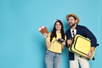 Photo of Tourism. Happy couple with passports, tickets and suitcase on light blue background, space for text