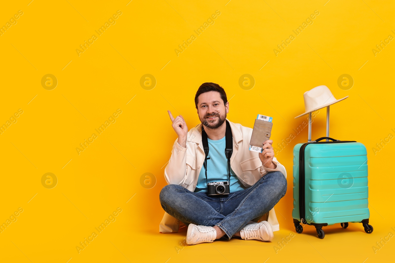 Photo of Traveller with vintage camera, passport, ticket and suitcase on orange background, space for text