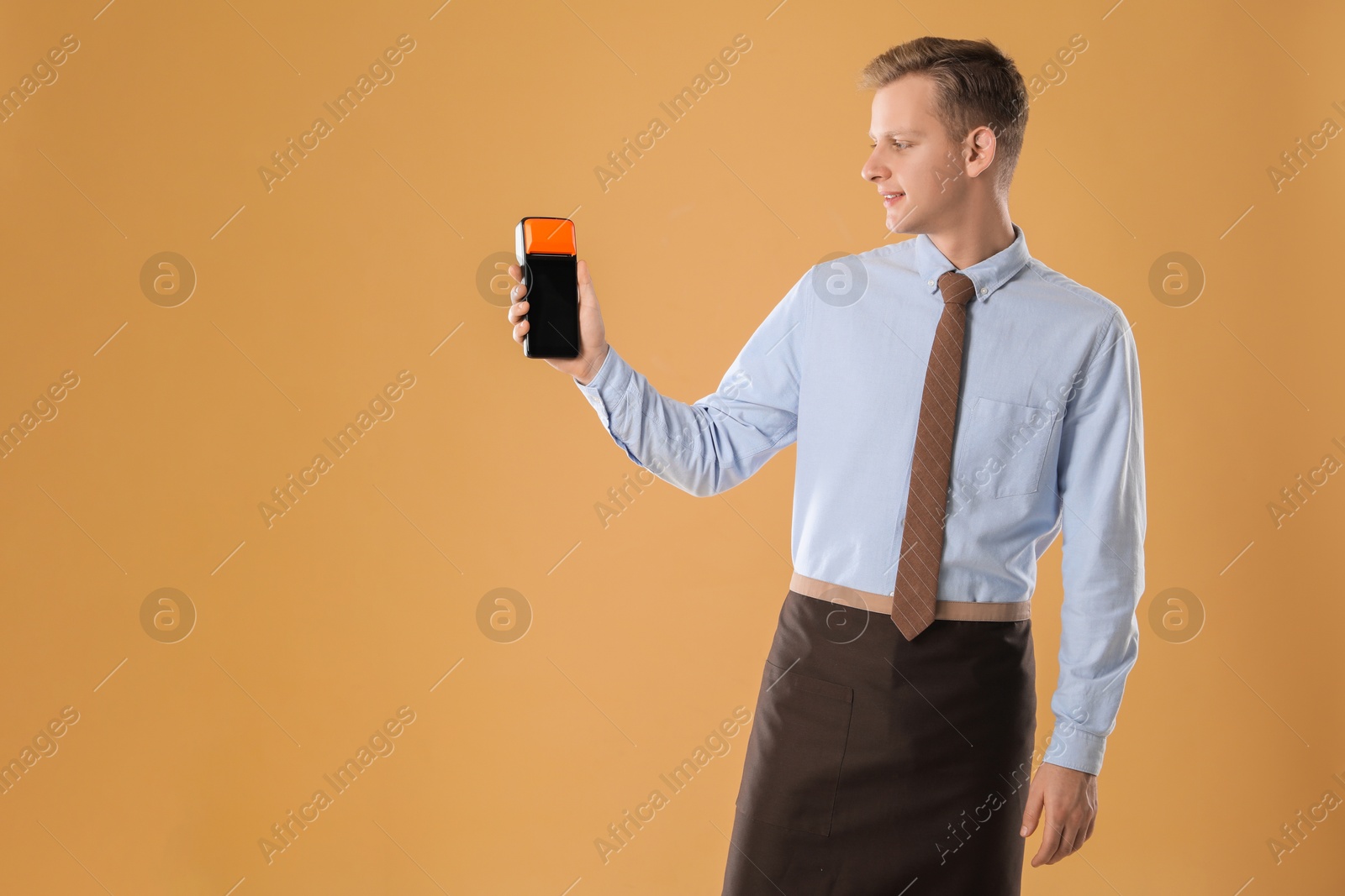 Photo of Happy young man with payment terminal on beige background, space for text