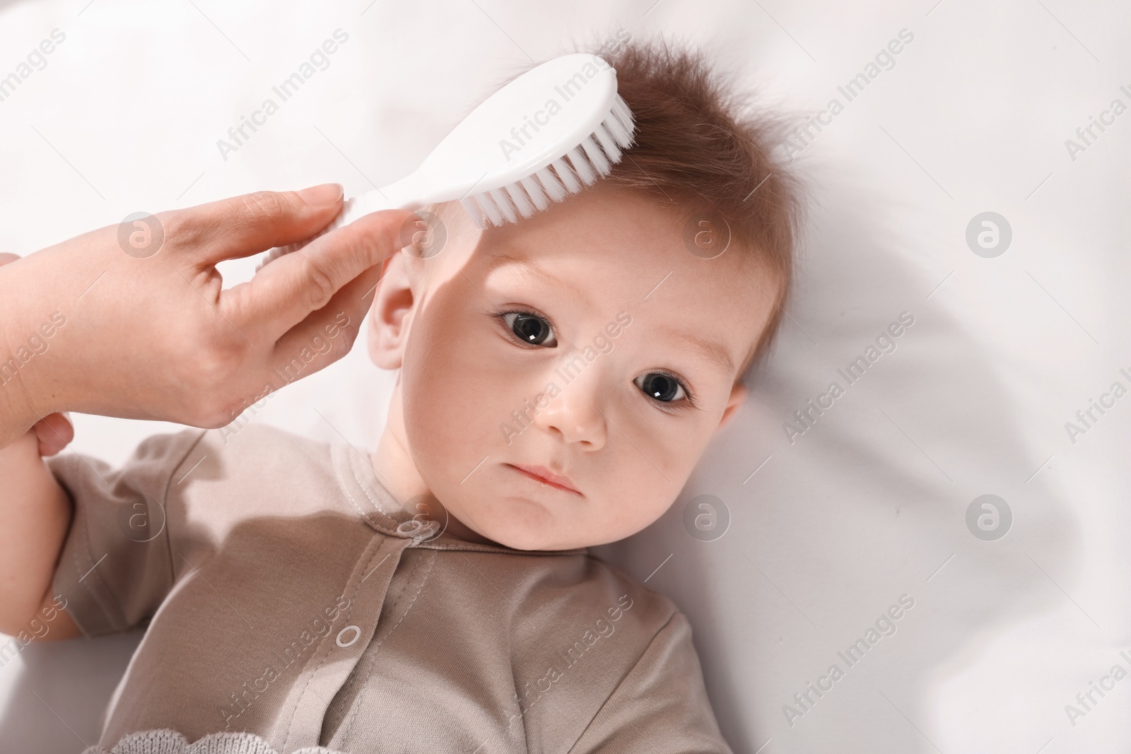 Photo of Woman brushing hair of her little baby indoors, top view. Space for text