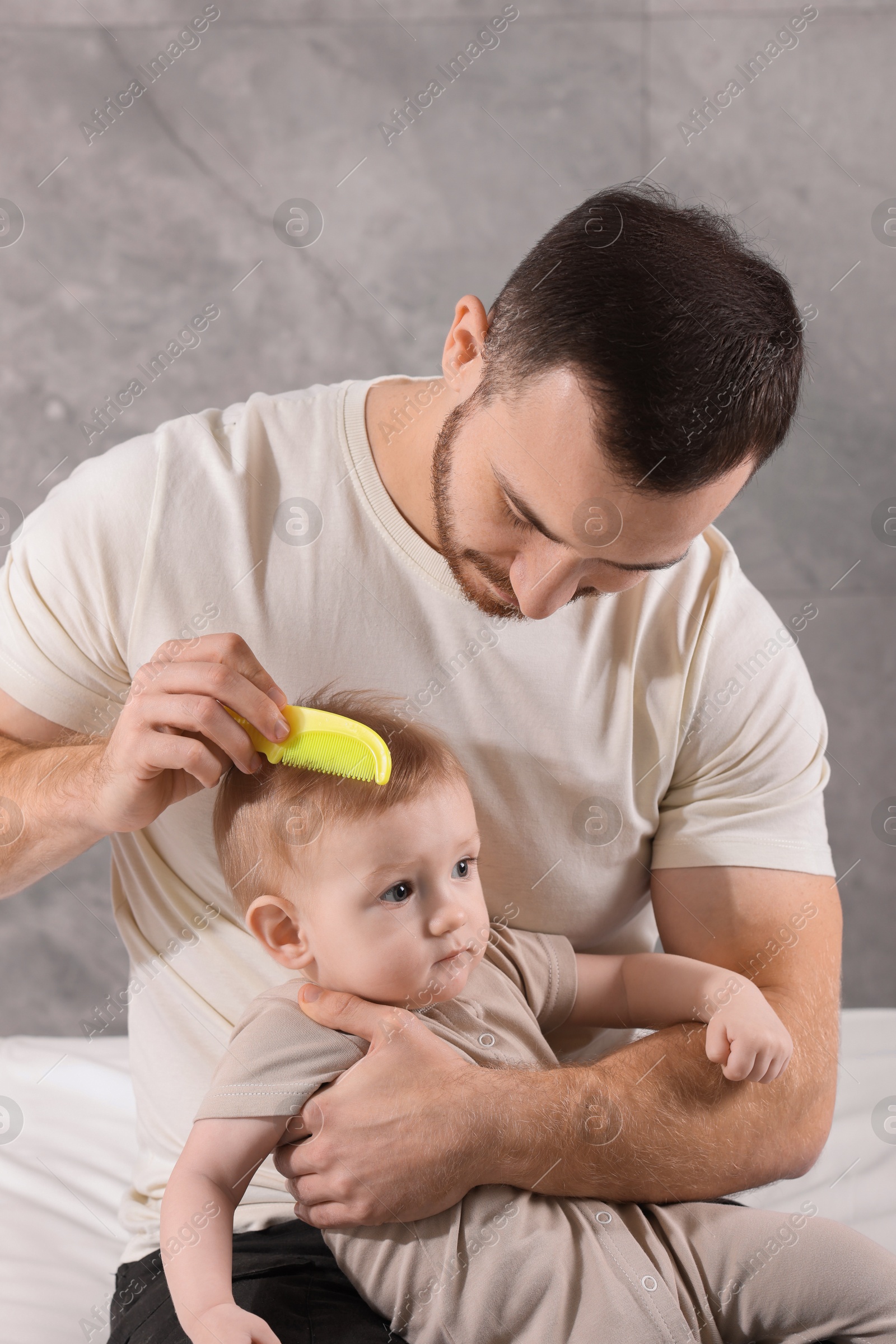 Photo of Man brushing hair of his little baby on bed indoors