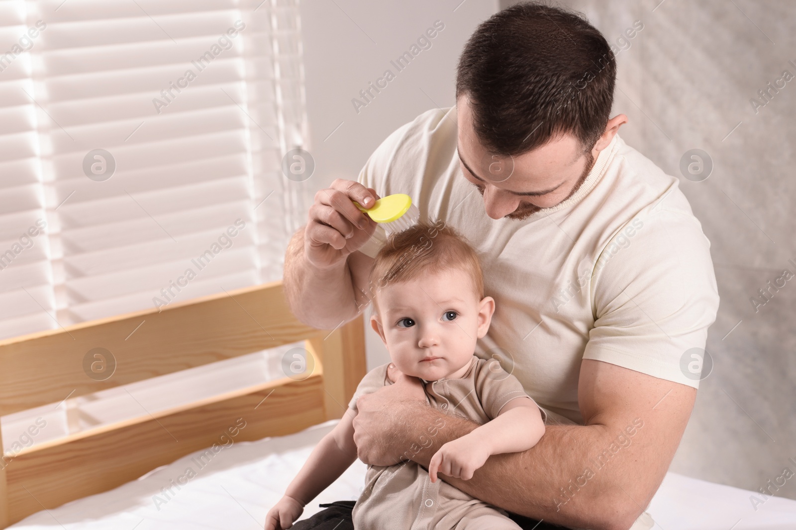 Photo of Man brushing hair of his little baby on bed indoors, space for text