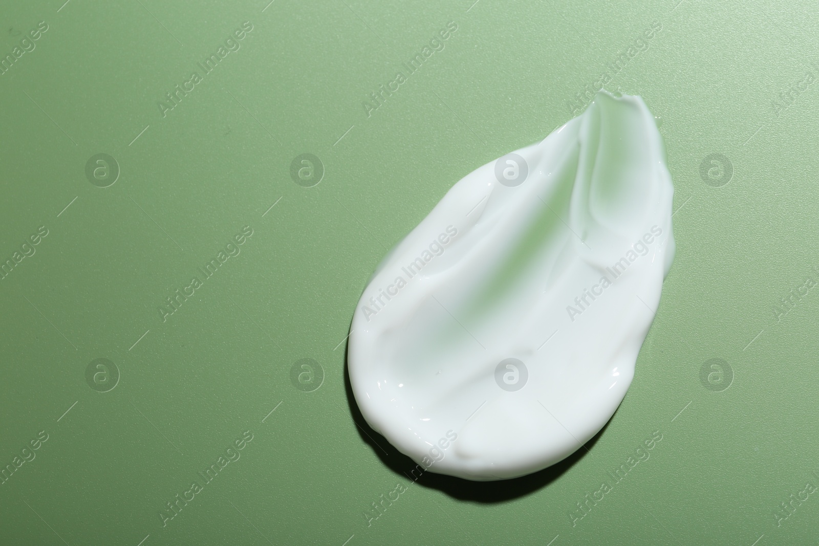 Photo of Cream on green background, top view and space for text. Sample of skincare product