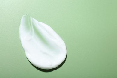 Photo of Cream on green background, top view and space for text. Sample of skincare product