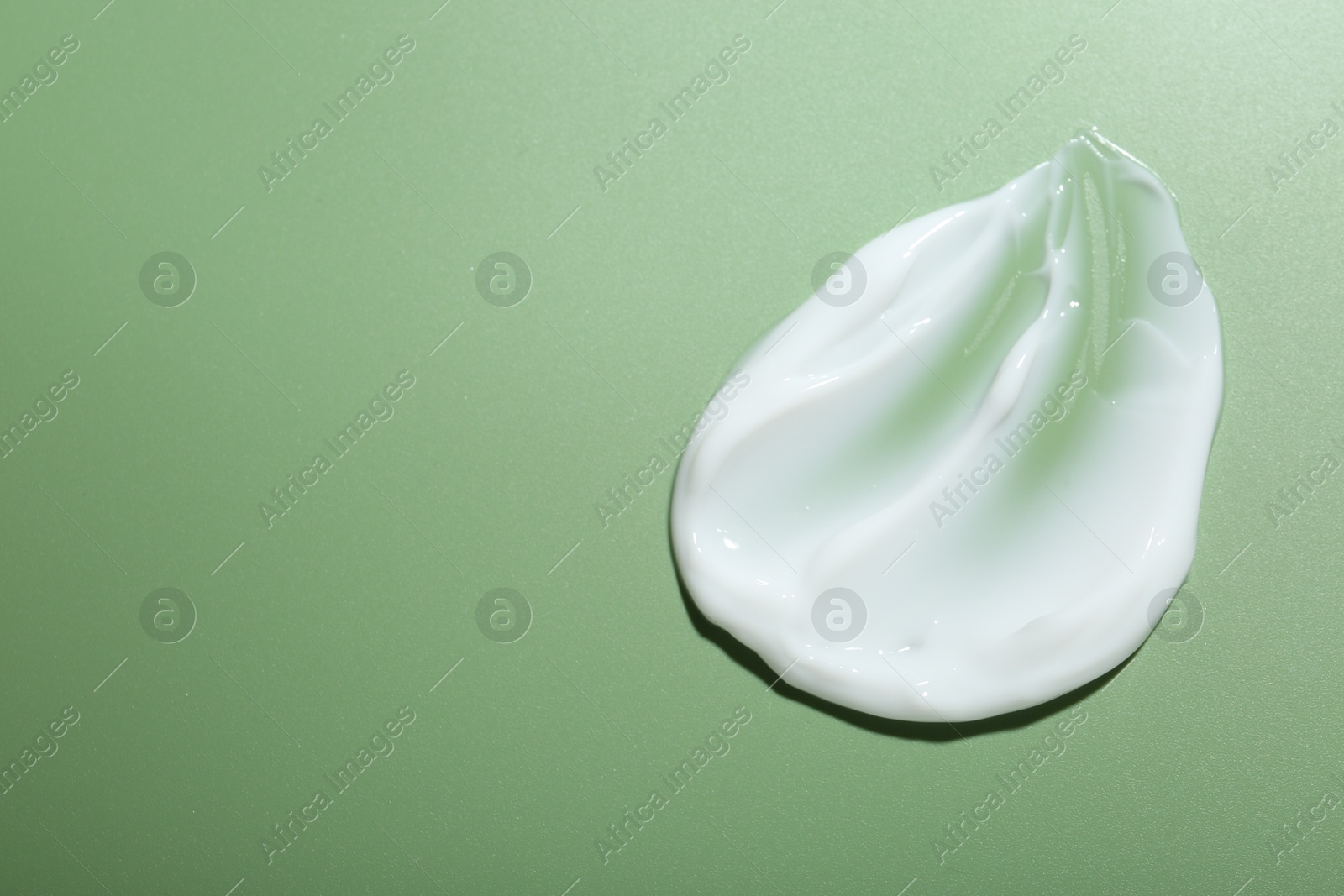 Photo of Cream on green background, top view and space for text. Sample of skincare product