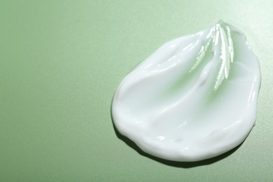 Photo of Cream on green background, closeup. Sample of skincare product