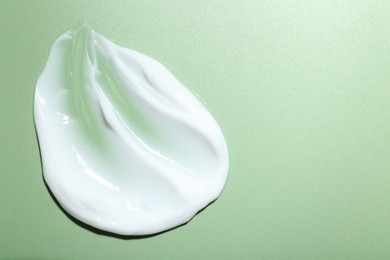 Photo of Cream on green background, top view and space for text. Sample of skincare product