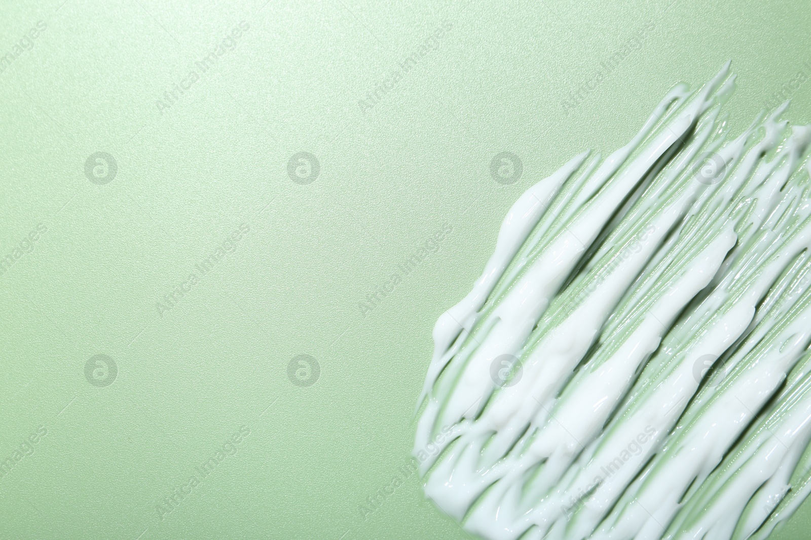 Photo of Cream on green background, top view and space for text. Sample of skincare product