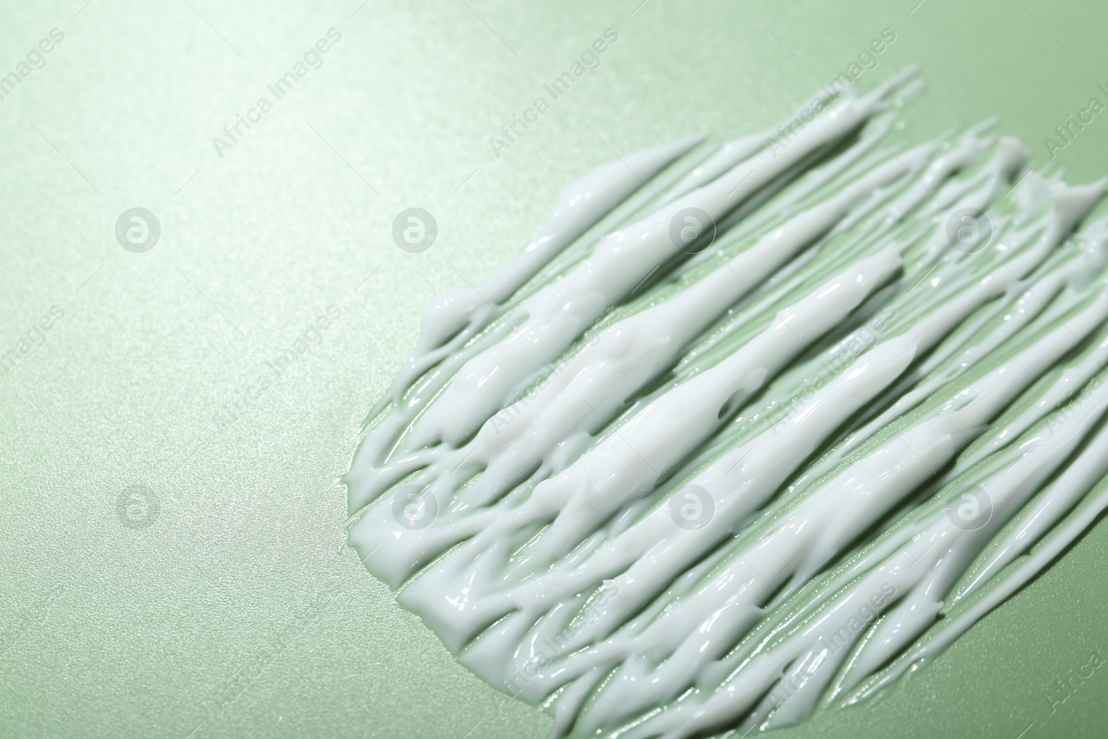 Photo of Cream on green background, closeup. Sample of skincare product