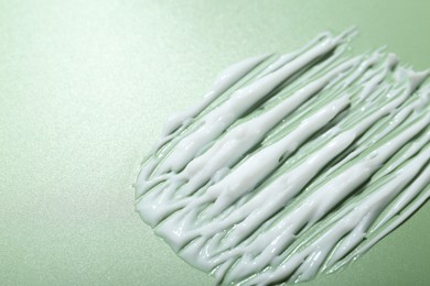 Photo of Cream on green background, closeup. Sample of skincare product