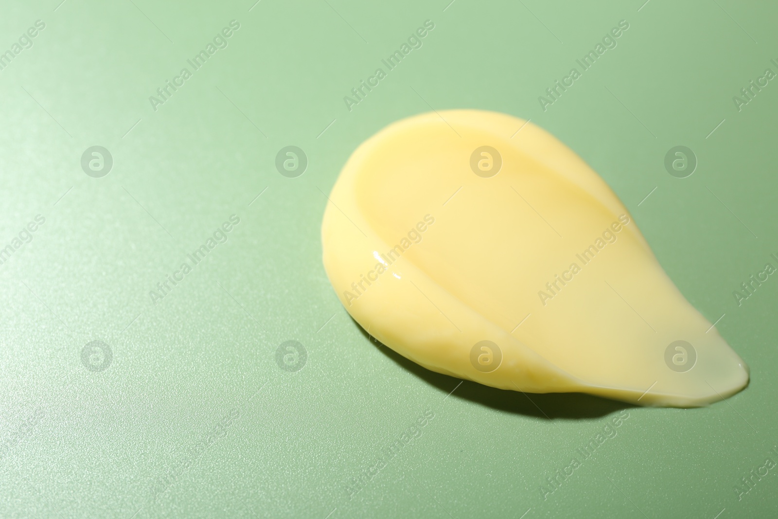 Photo of Cream on green background, closeup. Sample of skincare product