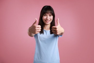 Photo of Happy woman showing thumbs up on pink background. Like gesture