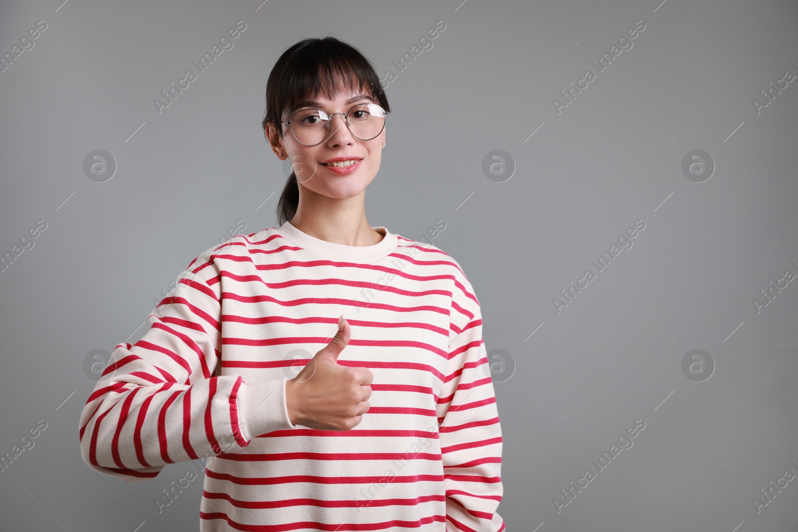 Photo of Happy woman showing thumbs up on grey background, space for text. Like gesture