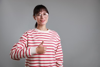 Photo of Happy woman showing thumbs up on grey background, space for text. Like gesture