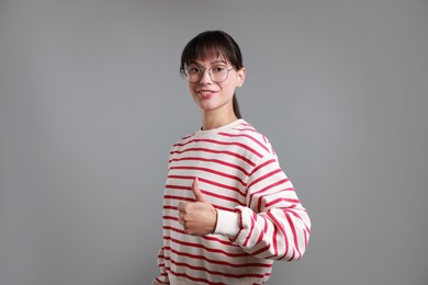 Photo of Happy woman showing thumbs up on grey background. Like gesture