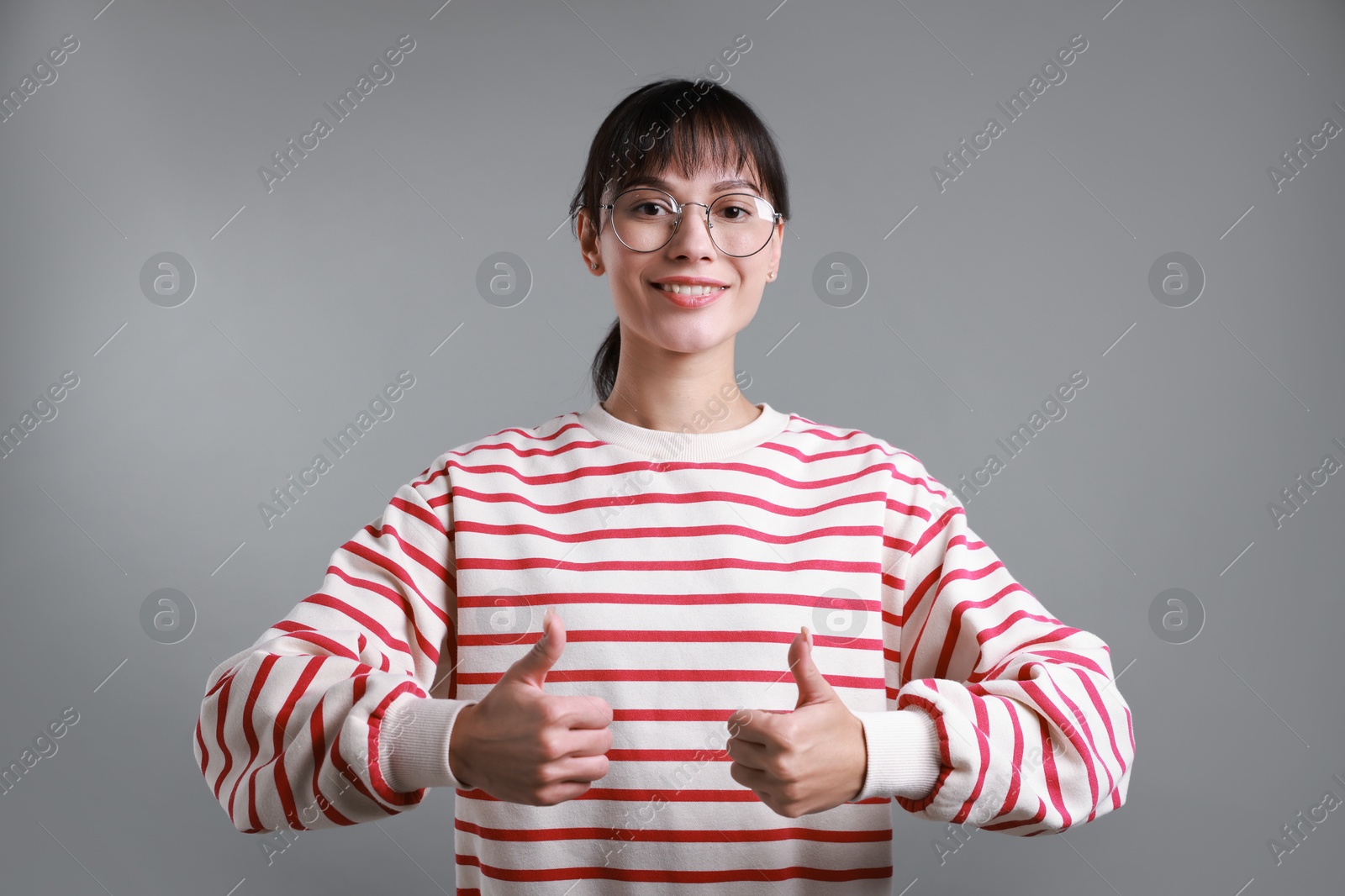 Photo of Happy woman showing thumbs up on grey background. Like gesture